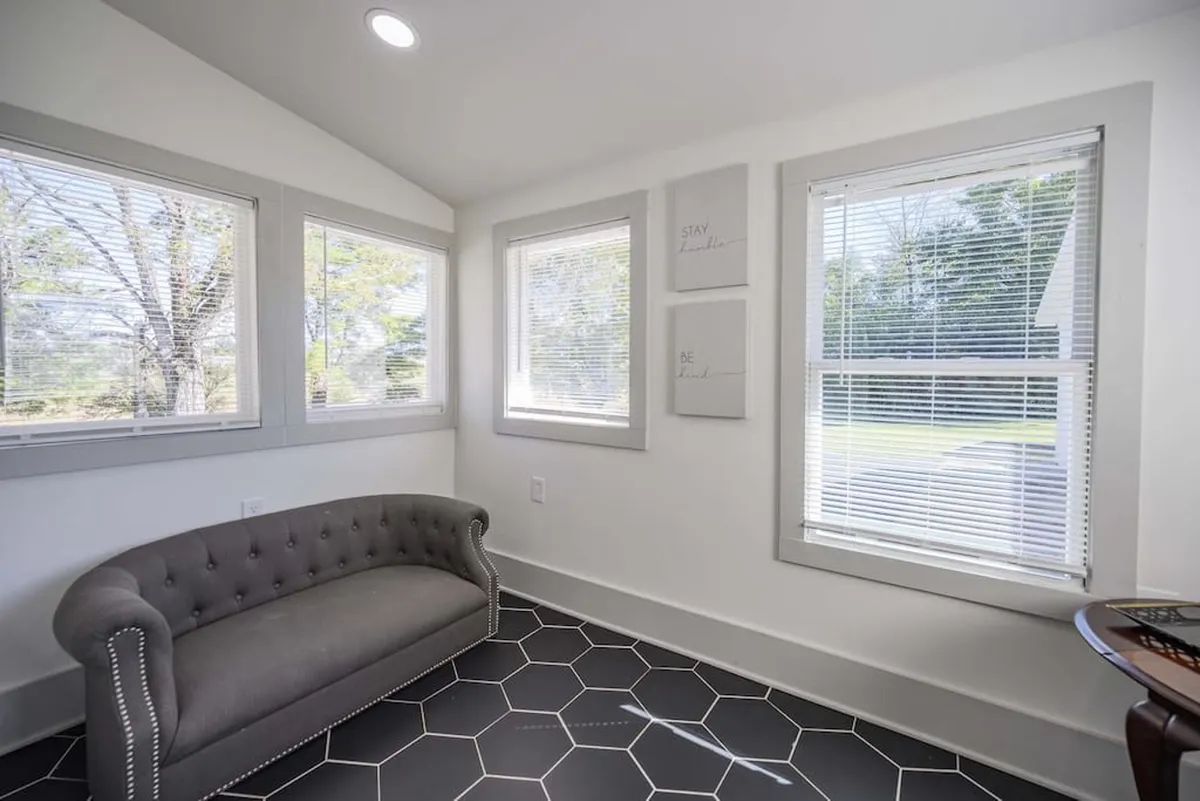 A serene sitting area with a gray tufted sofa, hexagonal tile flooring, and decorative wall art. The space is designed for tranquility, ideal for moments of solitude or creative inspiration.
