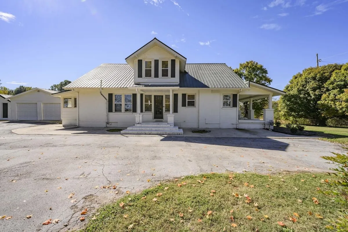 This image captures the welcoming exterior of the home, featuring a spacious front porch with a gabled roof, large windows, and a beautifully landscaped yard. The inviting porch offers a great spot to relax and watch sunsets or greet neighbors, reflecting the friendly, small-town atmosphere described in the section.