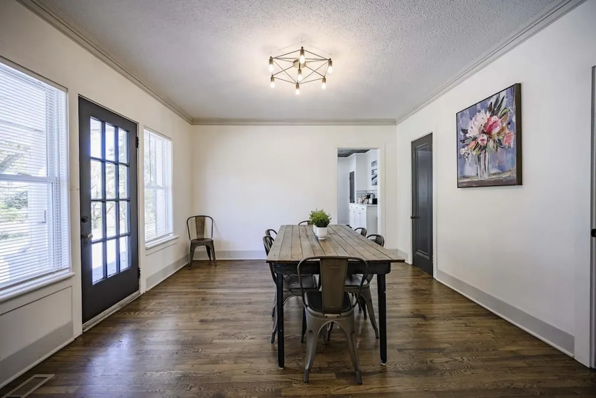 A long wooden dining table surrounded by metal chairs, with artwork and a contemporary light fixture overhead. The space is set for family gatherings, shared meals, and lively conversation, radiating a welcoming and modern atmosphere.