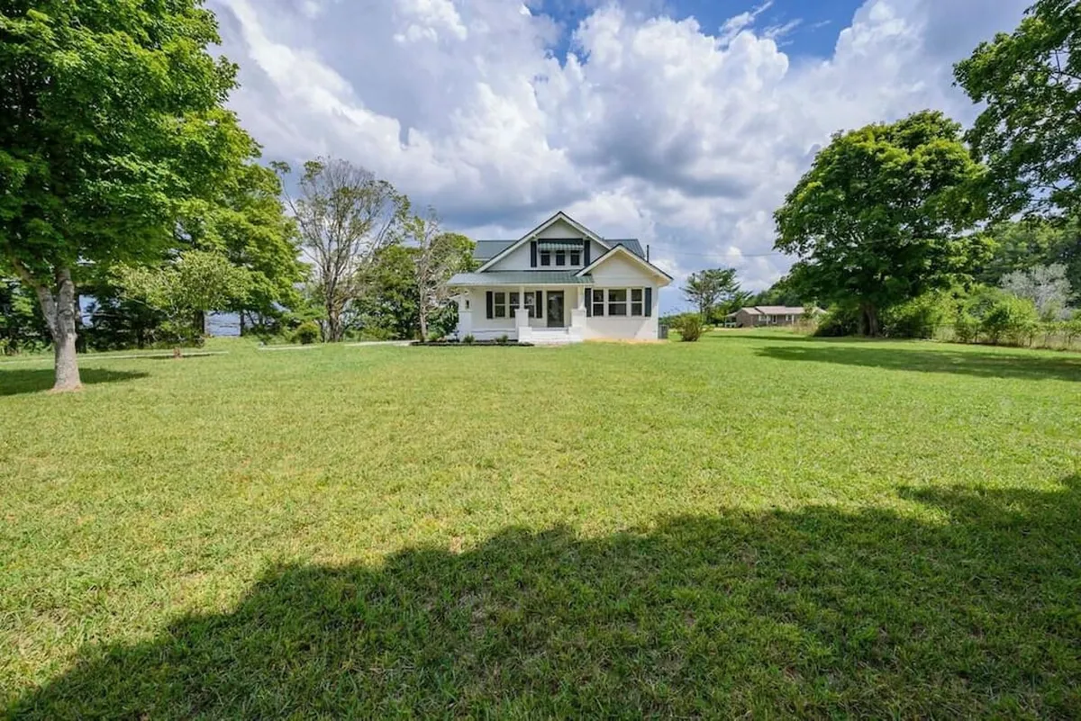 An expansive, tree-framed lawn stretches out before the house, offering open space for picnics, outdoor games, or quiet reflection. The lawn captures the essence of a private, peaceful retreat ideal for families or groups.
