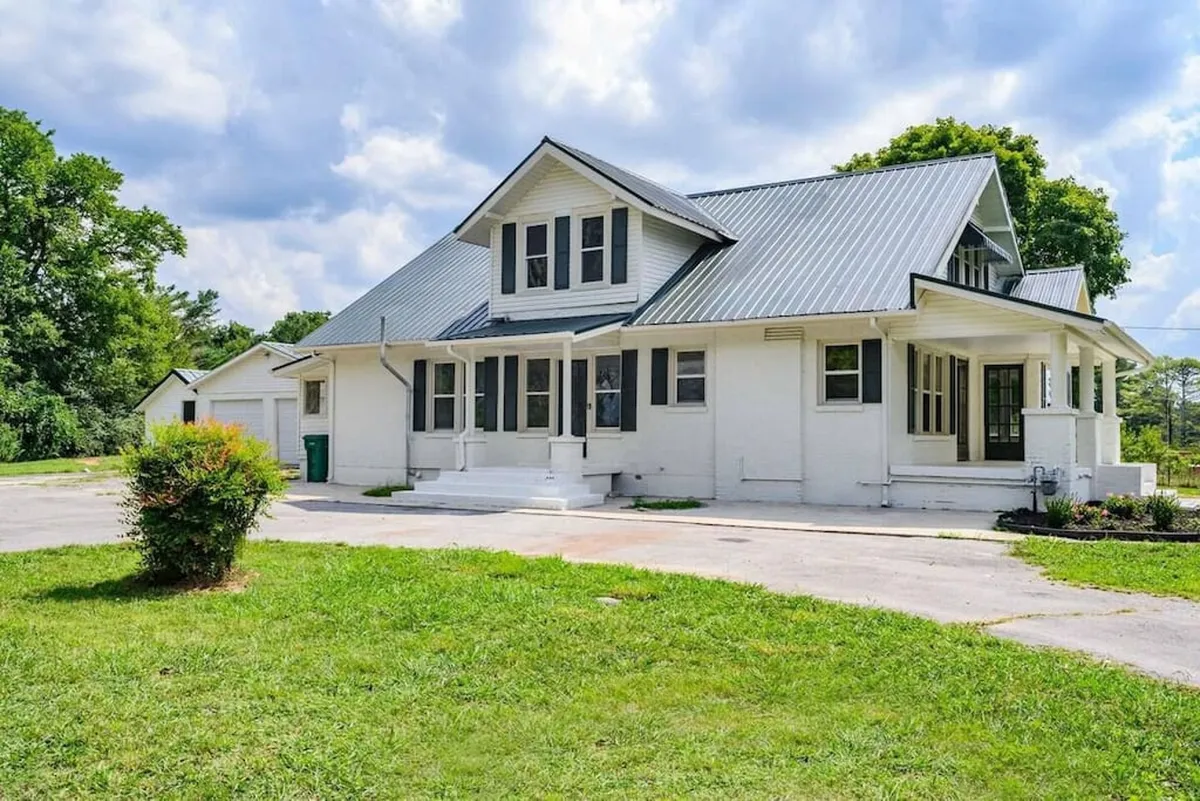 A large front porch fronts a charming farmhouse, with broad steps leading down to a well-kept green lawn. The porch is perfectly oriented for sunset views, and the lawn offers ample space for family games and gatherings.
