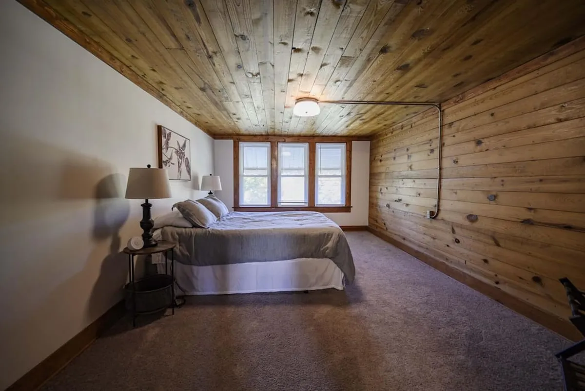 A bright bedroom featuring a comfortable bed, large windows letting in natural light, stylish lamps, and tasteful artwork. The space feels airy and tranquil, with a balance of modern touches and inviting textures.