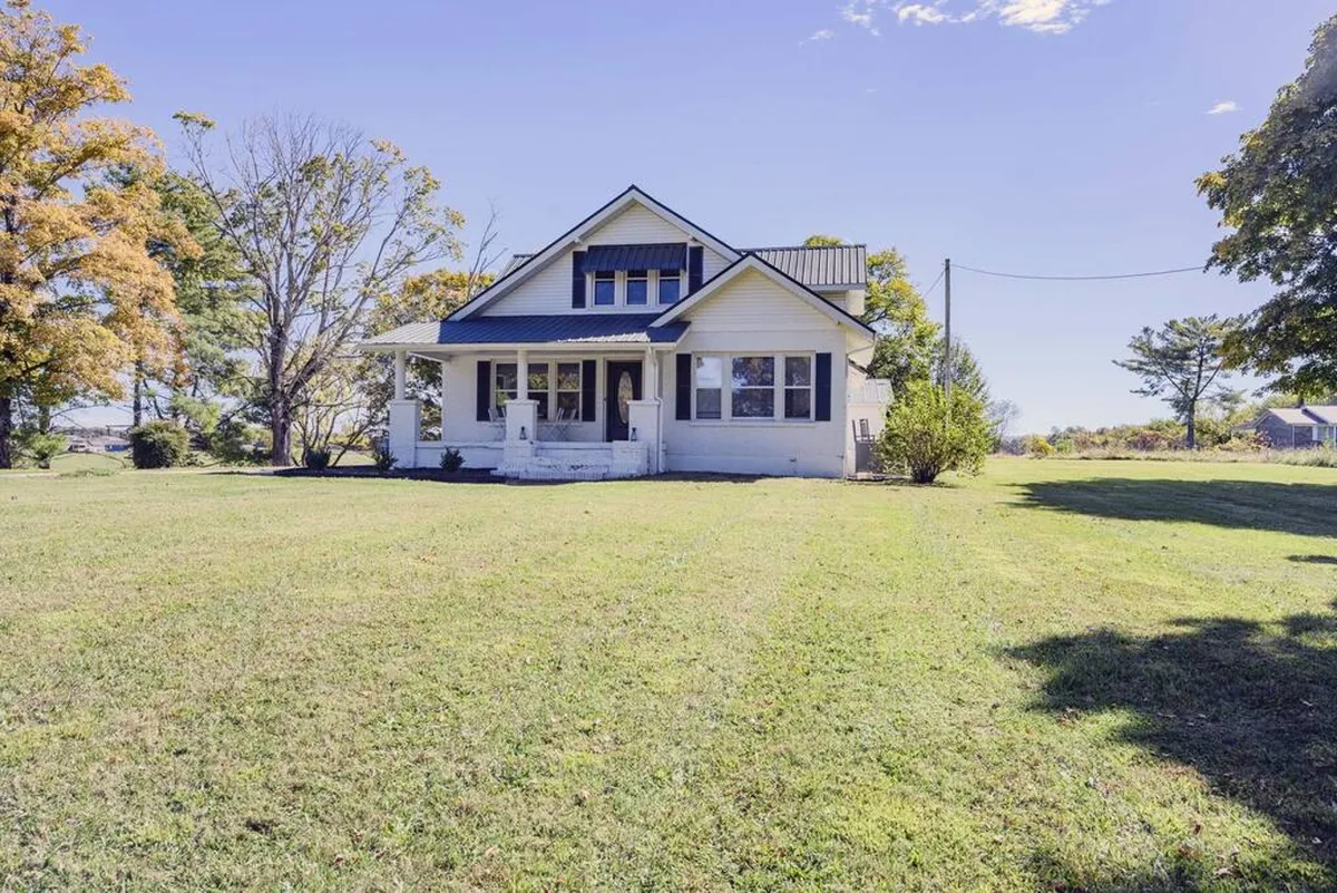 A view of the historic house from the outside, with a prominent front porch and surrounded by mature trees. The inviting scene hints at space for family gatherings and relaxation after a day at the lake.