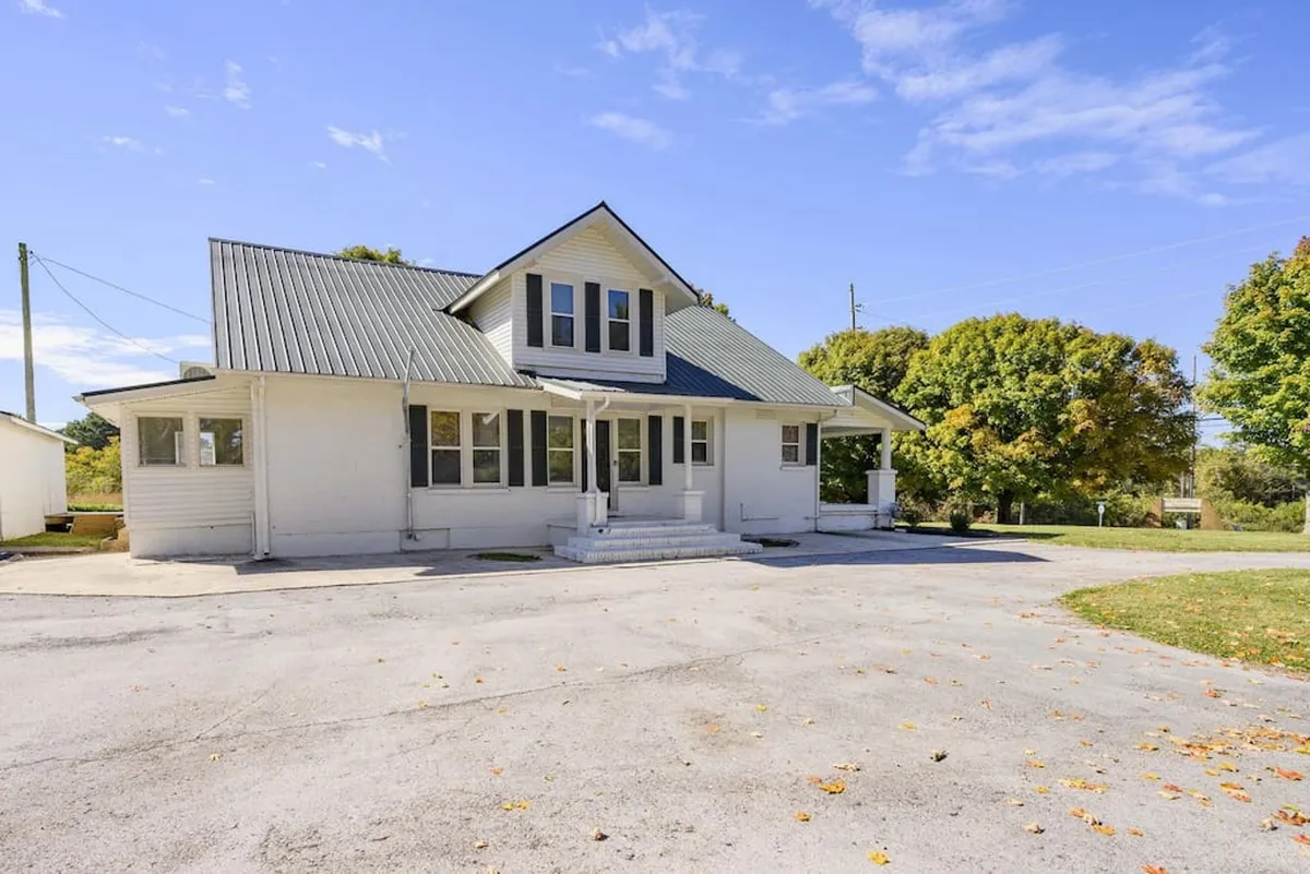 Showcasing the house’s classic gabled roof, expansive front porch, and mature trees, this image situates the home within its lush, tree-lined context. The composition hints at opportunities for outdoor gatherings, evening strolls, and the natural beauty that surrounds Winchester’s downtown.