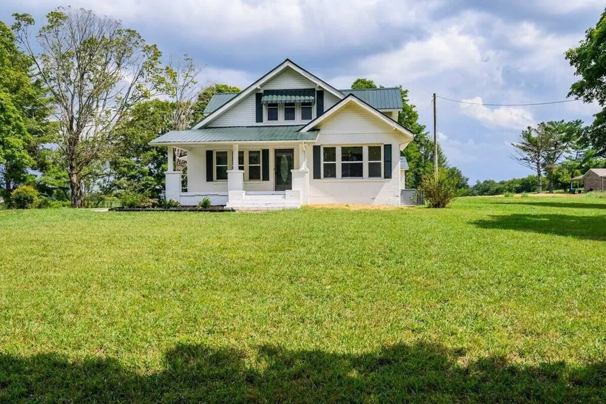 The image showcases the charming exterior of a beautifully renovated 1940s house, featuring a welcoming front porch perfect for relaxing. The lush green lawn offers ample space for family gatherings, outdoor play, and enjoying sunsets, embodying a serene and inviting atmosphere.