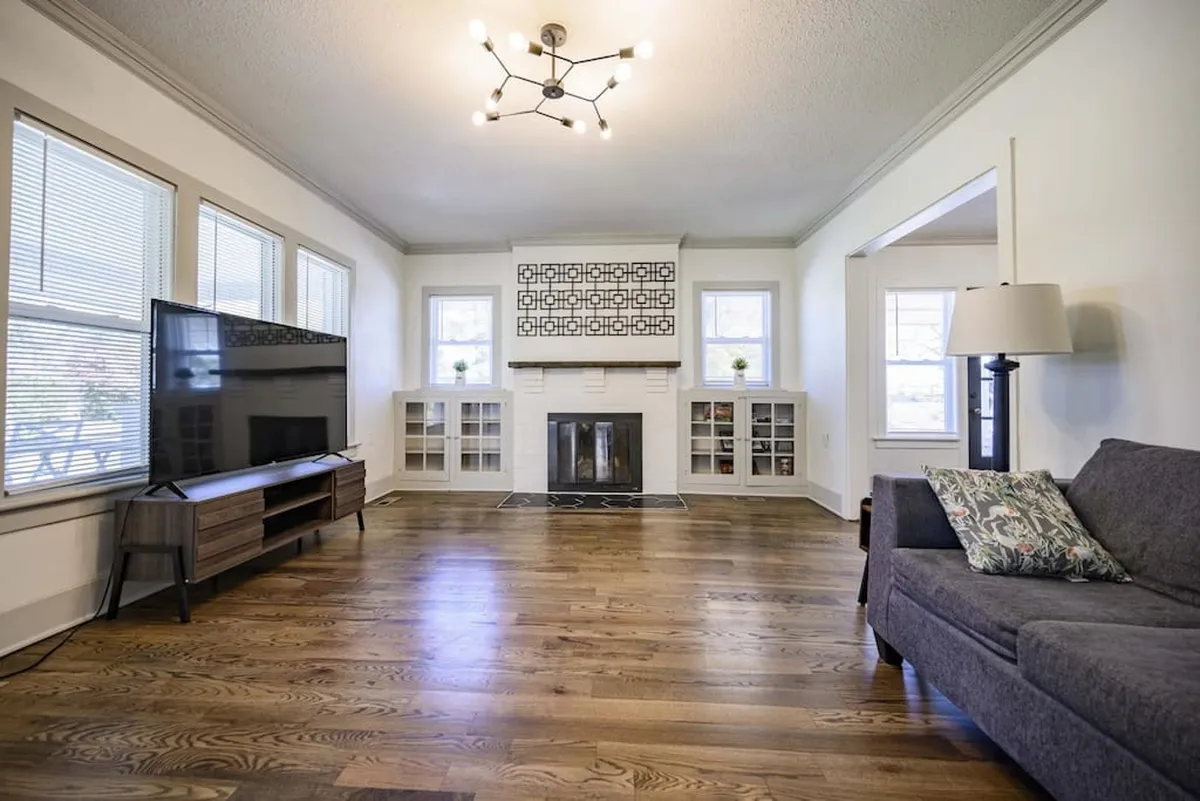 A bright, open living room featuring a comfortable sofa, a fireplace, a large TV, and window seating. Natural light streams in, inviting guests to relax, socialize, or enjoy a group movie night. The setting is cozy and spacious, perfect for gatherings and entertainment.